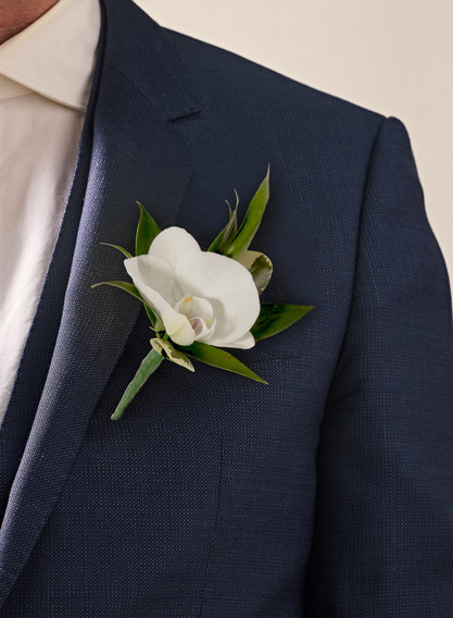 White rose boutonniere pinned to a navy suit lapel, elegant prom and wedding boutonniere detail.